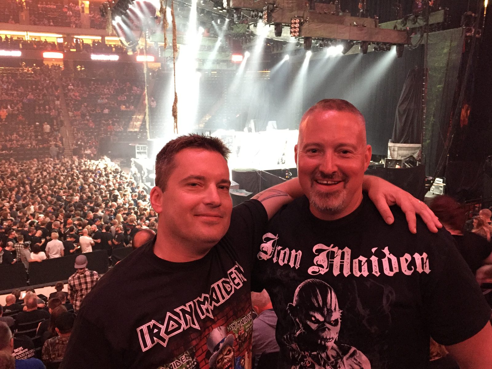 Two Iron Maiden fans at Xcel Energy Center, August 2019, with the stage and crowd behind them.
